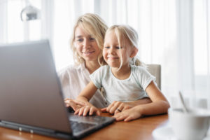 Smiling mother and child uses laptop at home. Parent feeling, togetherness, happy family